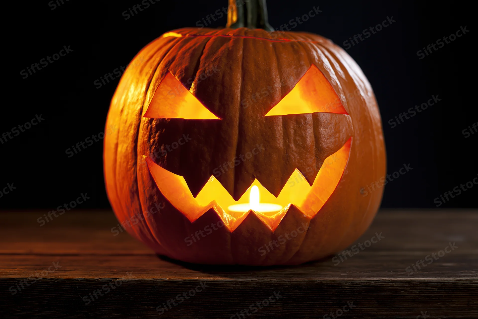 Carved pumpkin with glowing candle face on dark wooden surface