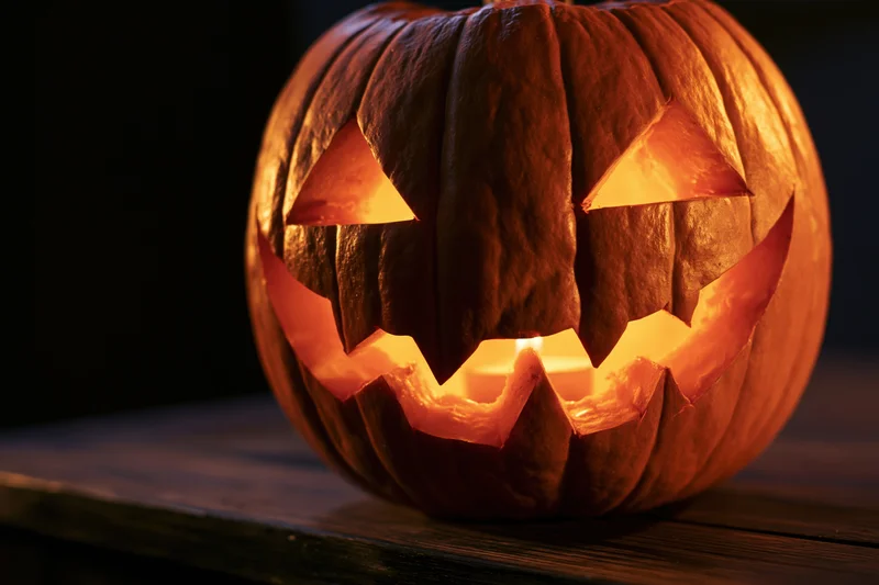 Carved pumpkin with glowing face sitting on dark wooden table