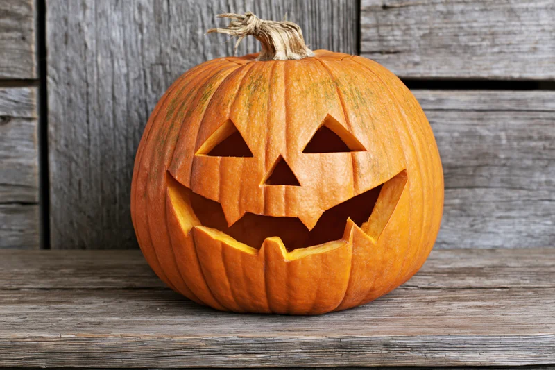 Carved pumpkin with triangular eyes and jagged grin resting on weathered wooden surface