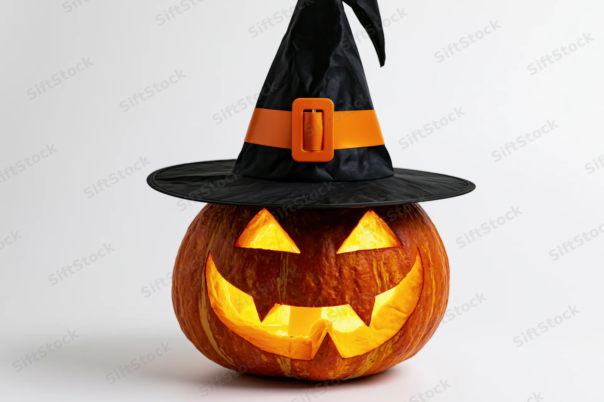 Carved pumpkin with glowing face wearing black witch hat on white background
