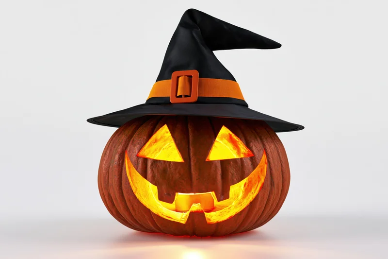Carved pumpkin with glowing face and witch hat on white background