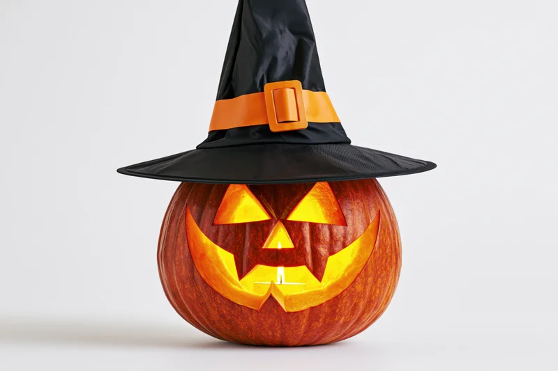 Carved pumpkin with glowing face and witch hat on white background