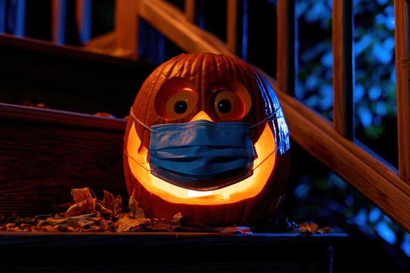 Carved pumpkin with blue surgical mask glowing on porch steps at night