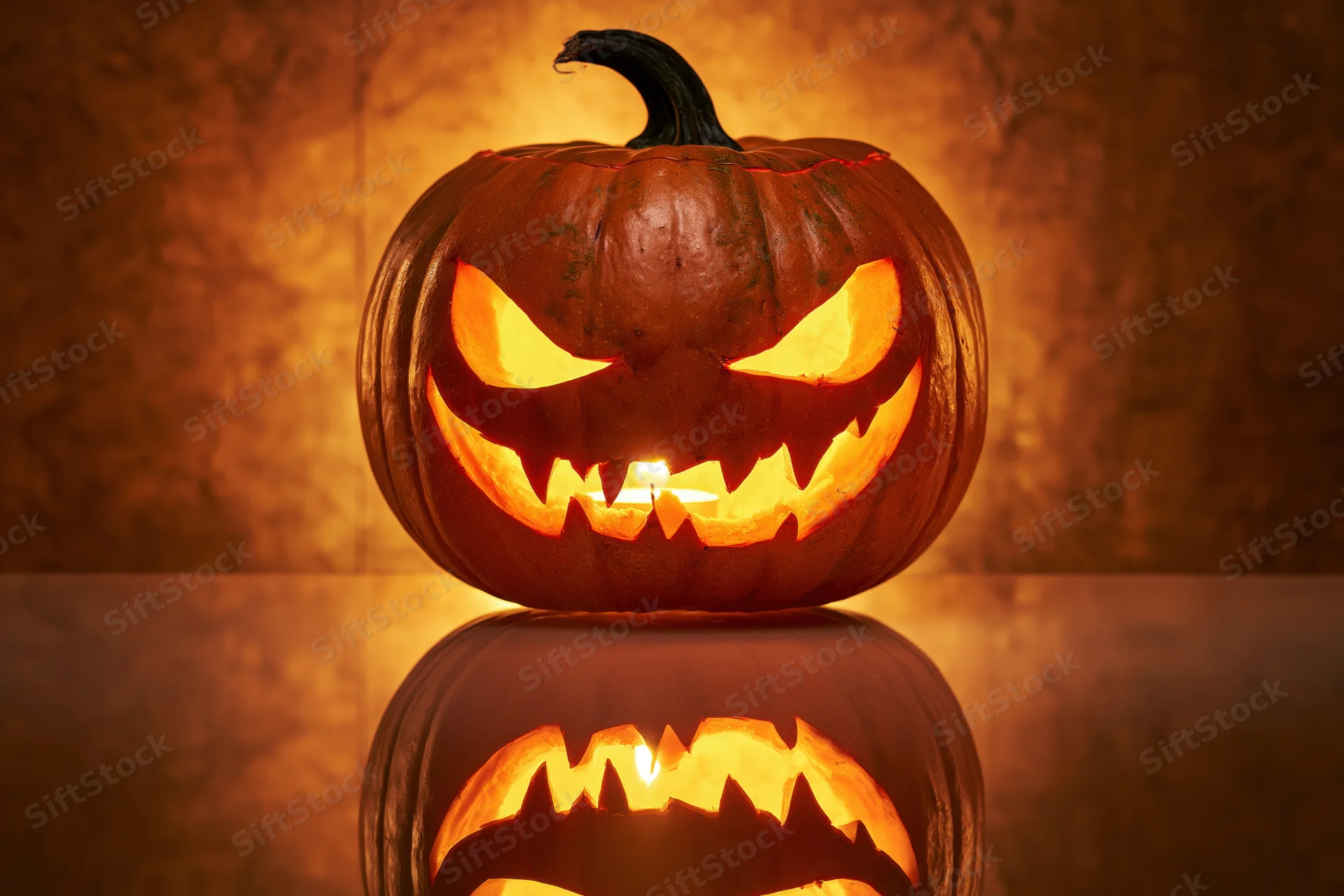 Carved pumpkin with glowing menacing grin reflecting on glass surface