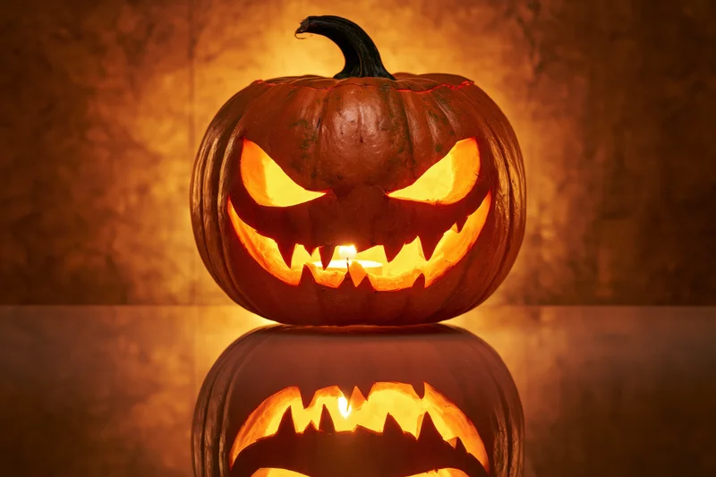 Carved pumpkin with glowing menacing grin reflecting on glass surface