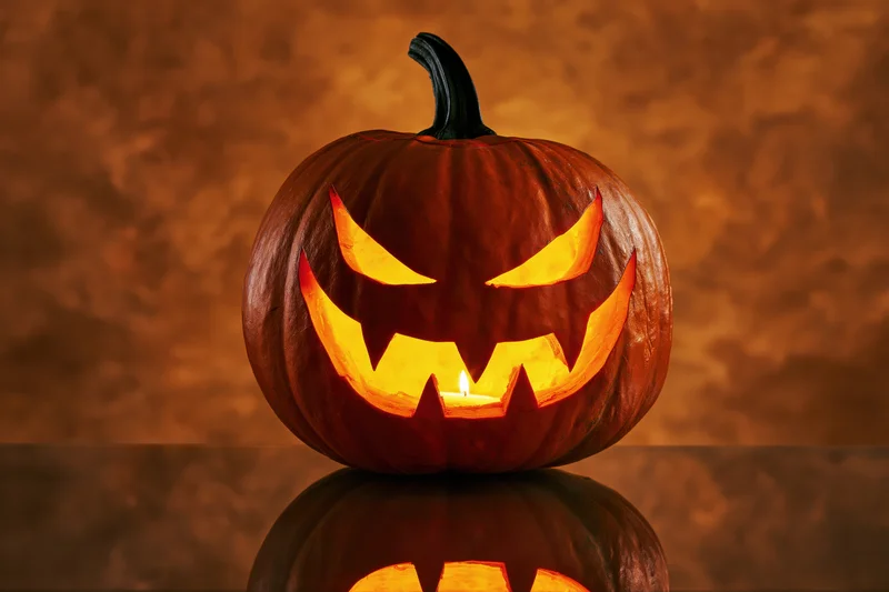 Carved pumpkin with glowing menacing grin on reflective surface