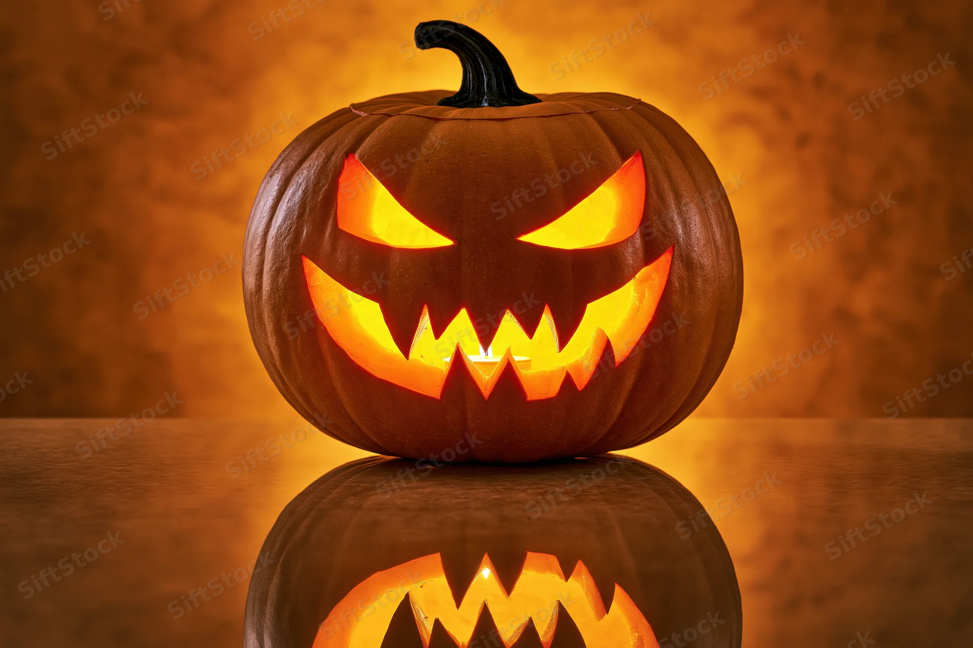 Carved pumpkin with glowing menacing grin on reflective surface