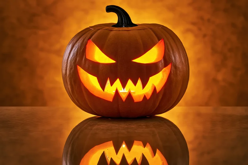 Carved pumpkin with glowing menacing grin on reflective surface