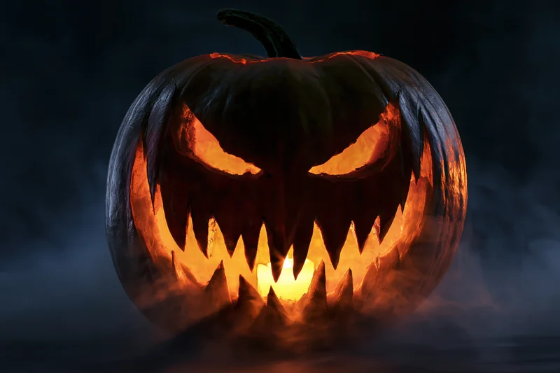 Carved pumpkin with jagged teeth and glowing eyes in dark smoky setting