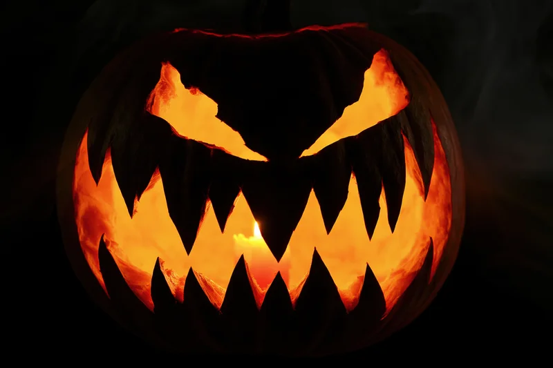 Carved pumpkin with jagged teeth and glowing eyes lit from within in dark smoky setting