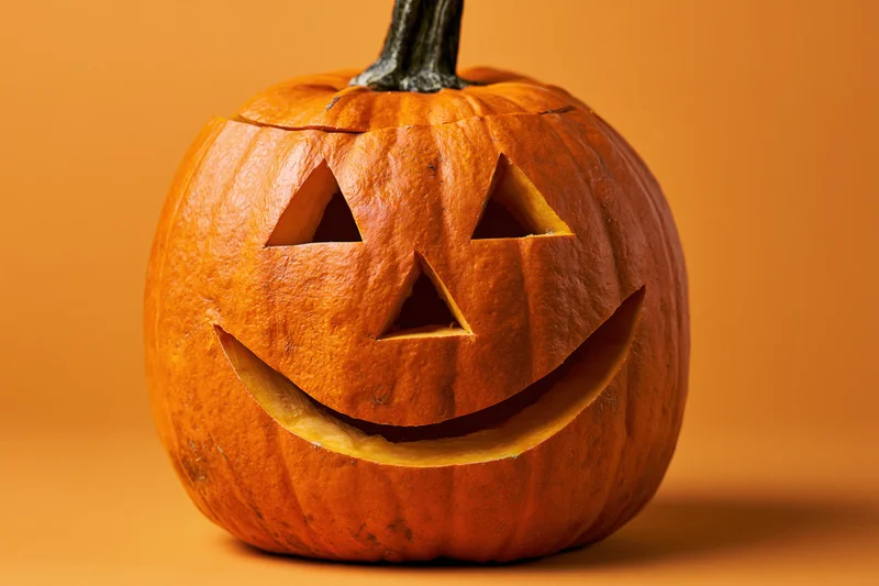 Carved pumpkin with smiling face on orange background