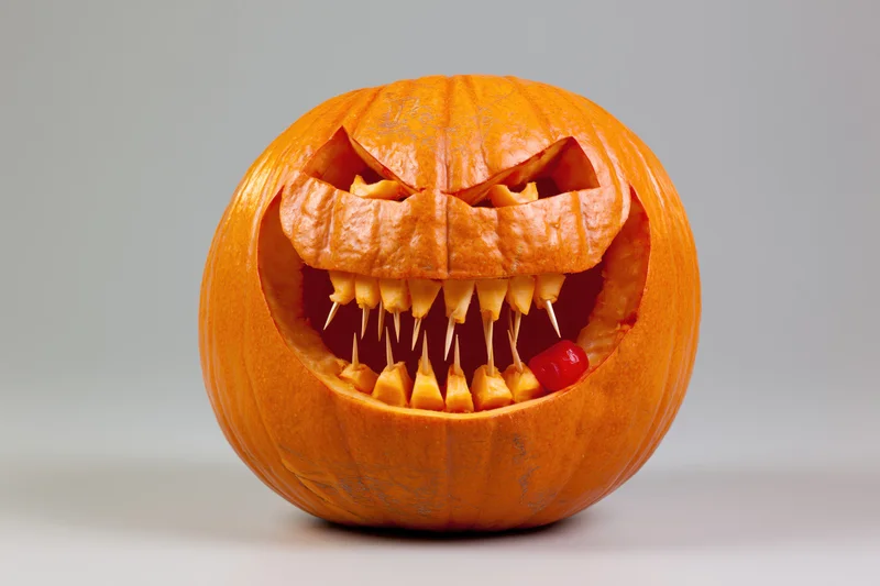 Carved pumpkin with jagged teeth and red candy in mouth on white background