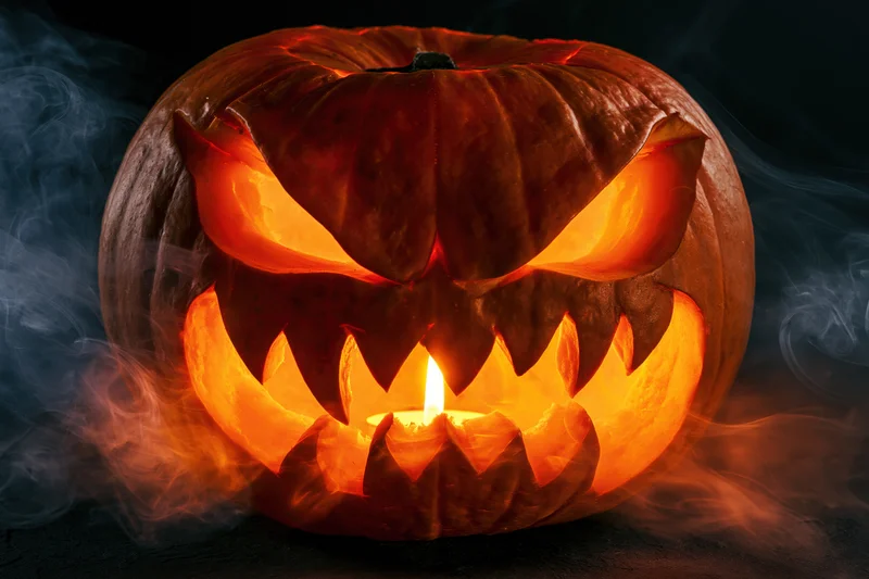 Carved pumpkin with glowing snarling face lit by candle surrounded by smoke