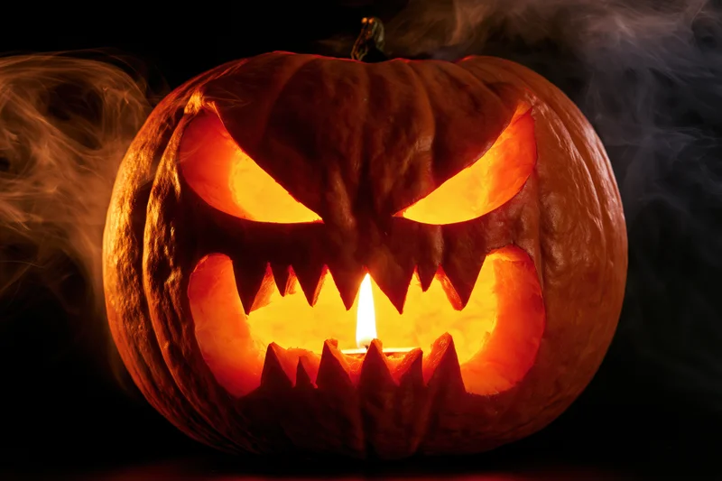 Carved pumpkin with glowing snarling face and smoke against dark background
