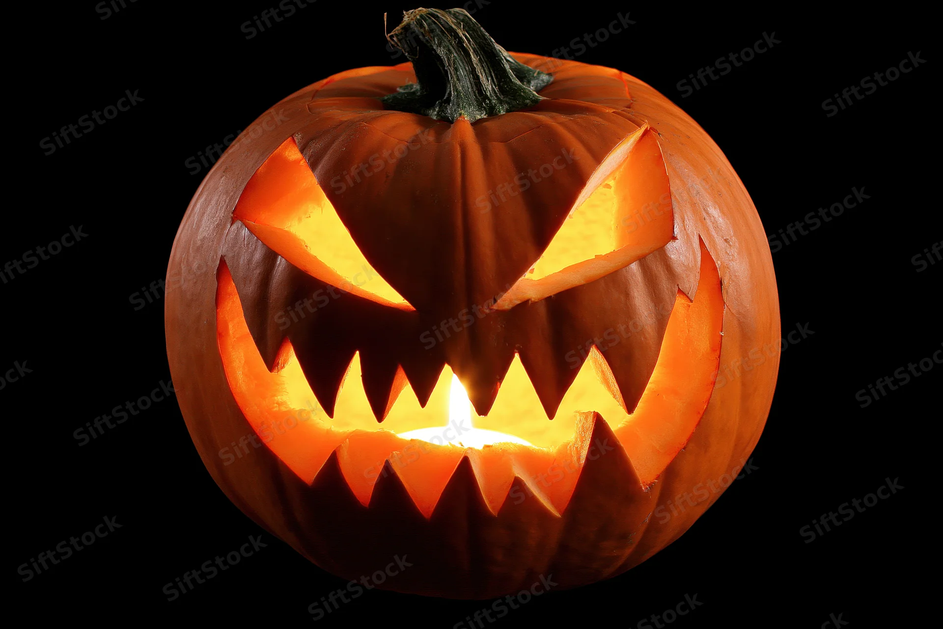 Carved pumpkin with jagged face lit from within against black background