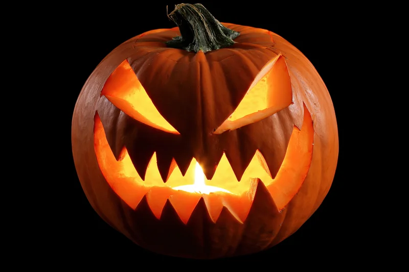Carved pumpkin with jagged face lit from within against black background
