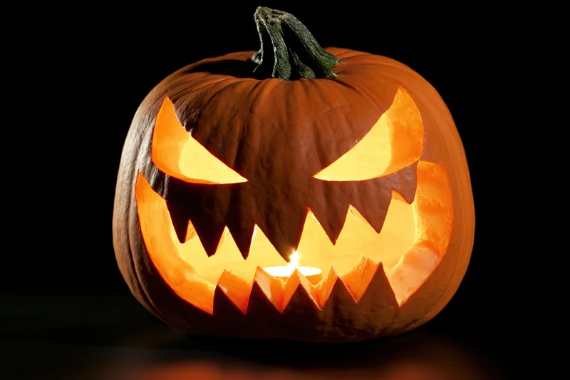 Carved pumpkin with jagged face lit by candle against black background