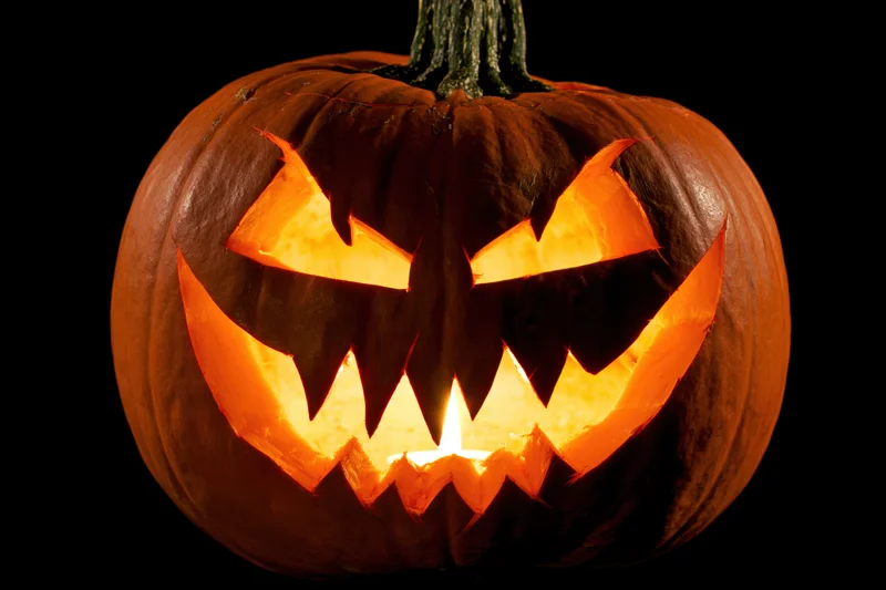 Carved pumpkin with jagged angry face illuminated from within against black background