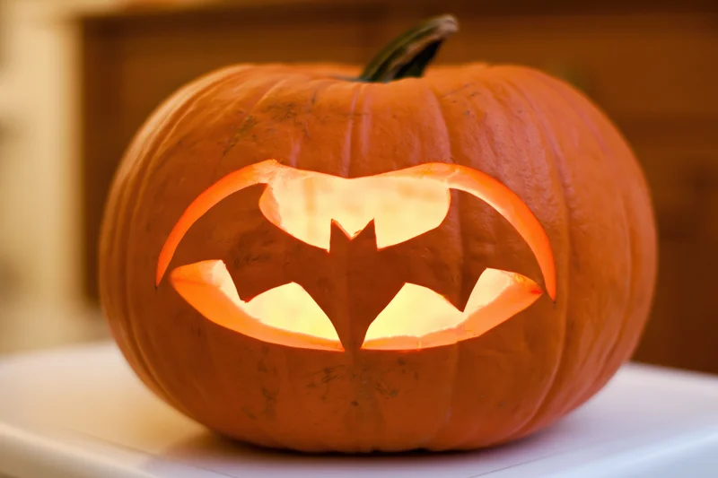 Carved pumpkin with bat face glowing on white surface