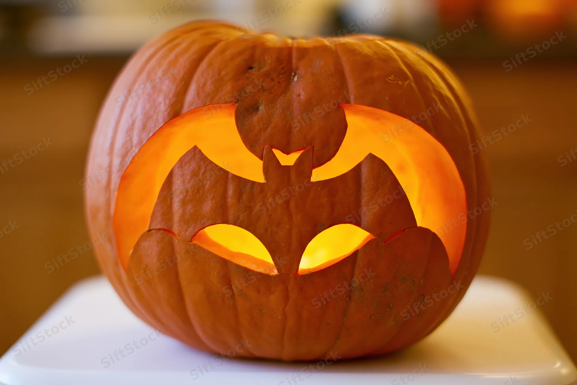 Carved pumpkin with bat design glowing on white surface