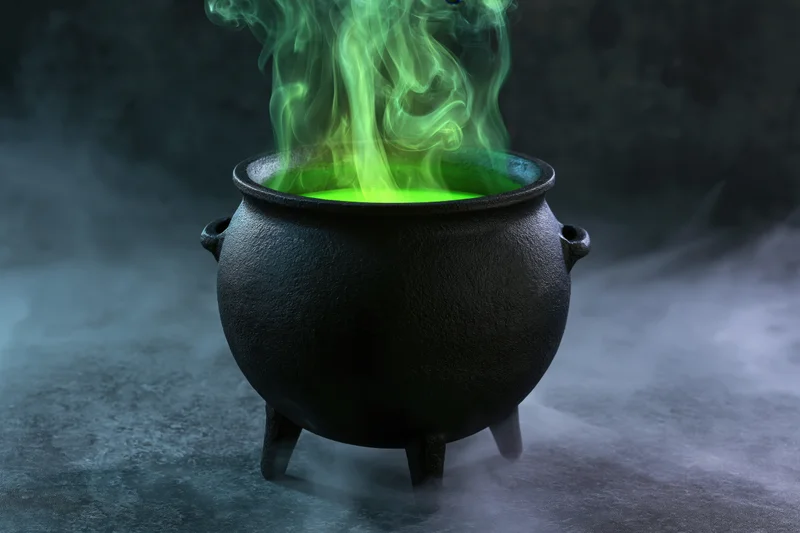 Black cast iron cauldron with glowing green liquid and rising smoke on a dark misty surface
