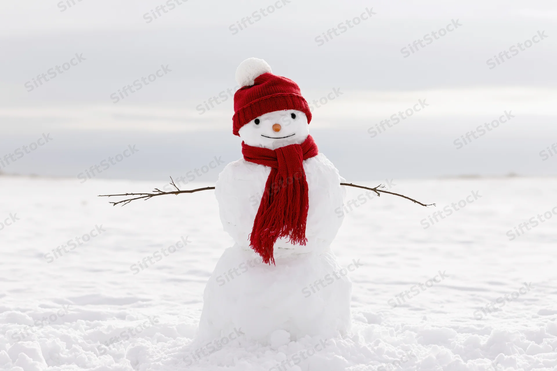 Cheerful snowman with red hat and scarf standing in open snow-covered field