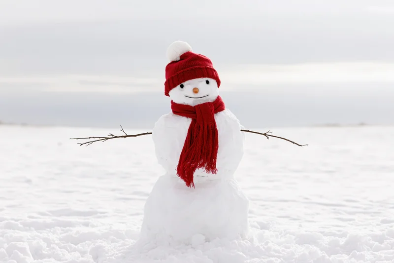 Cheerful snowman with red hat and scarf standing in open snow-covered field