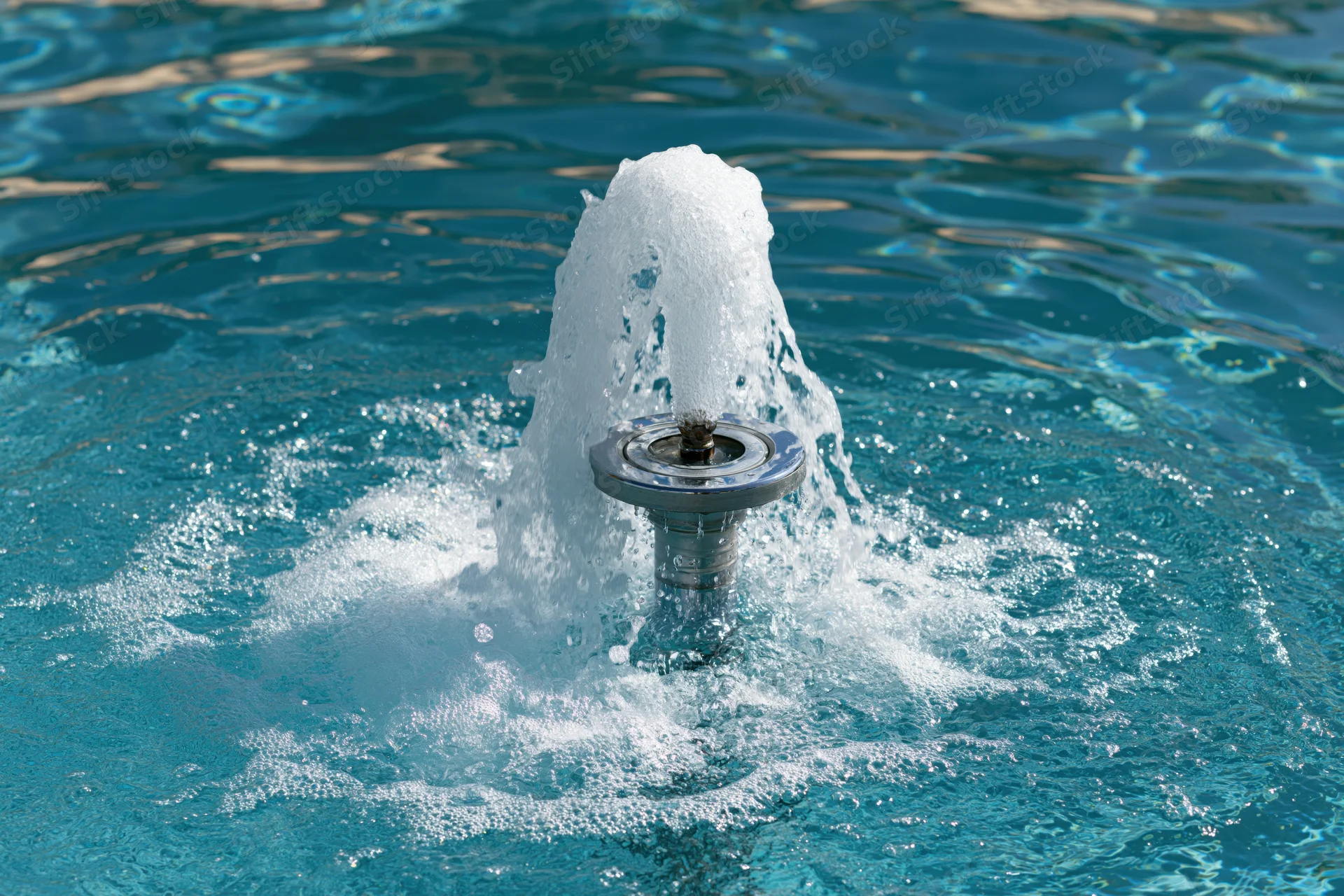 Chrome fountain jet spraying foamy water in a swimming pool