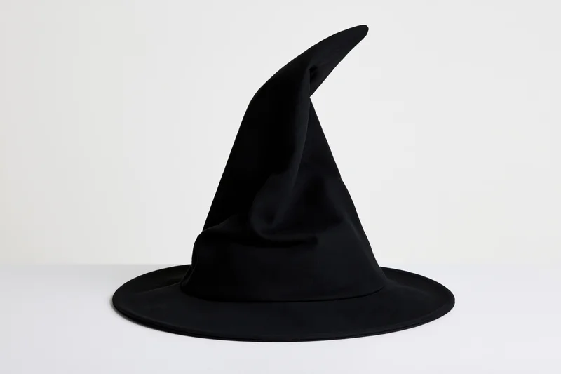 Black witch hat with tall curved pointed crown on white surface