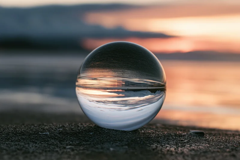 Crystal lensball resting on dark wet sand at beach during sunset reflecting sky and water