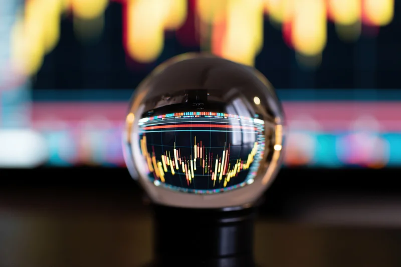 Crystal ball reflecting inverted stock market chart on a dark desk with blurred digital display in background