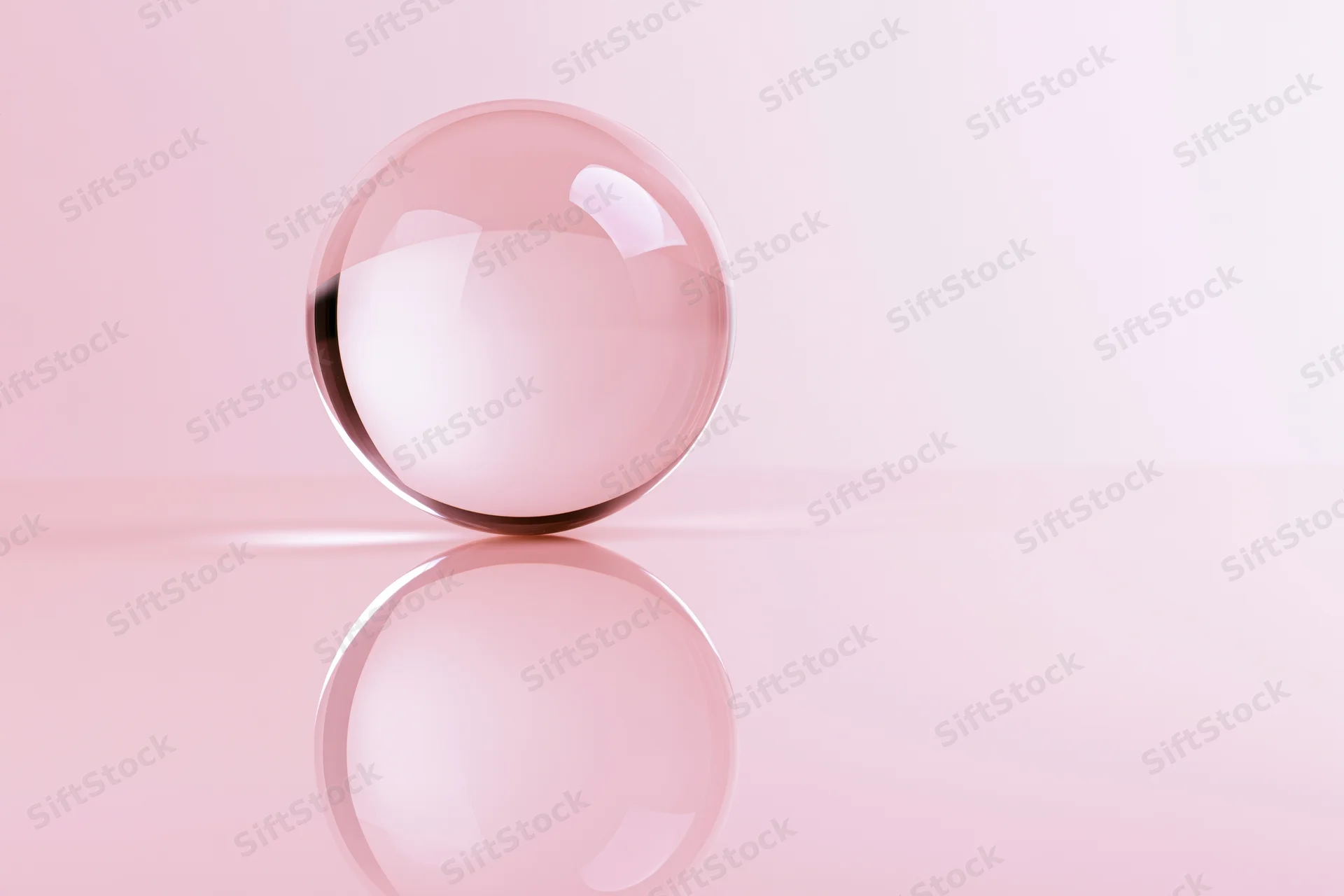 Clear glass crystal ball resting on glossy pink surface with reflection