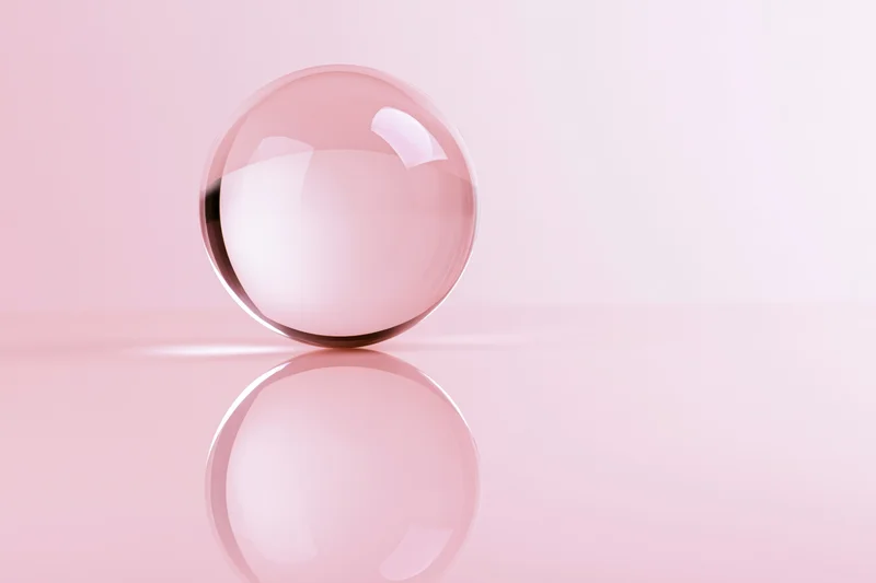 Clear glass crystal ball resting on glossy pink surface with reflection