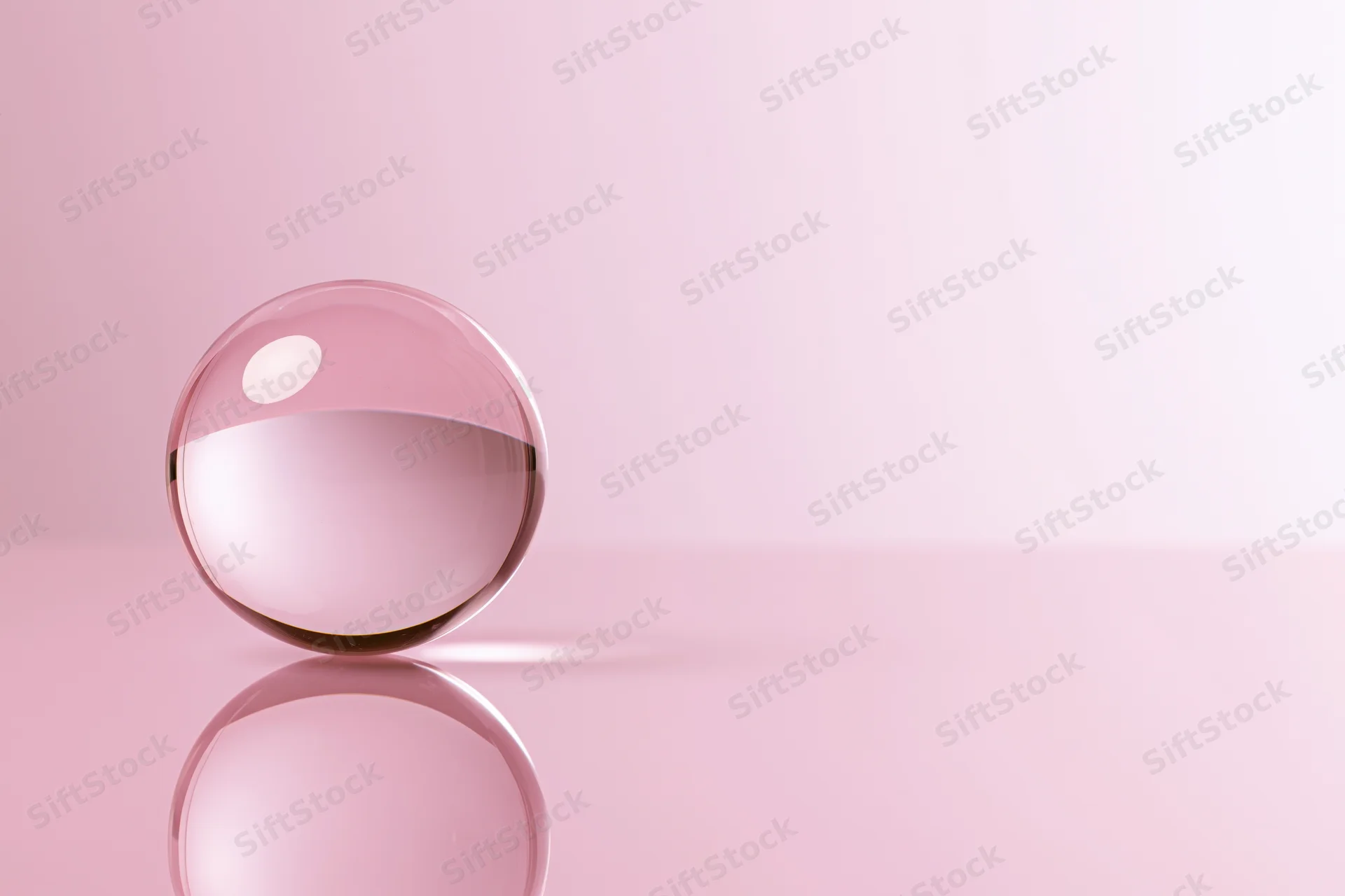 Clear glass crystal ball resting on glossy pink surface with reflection