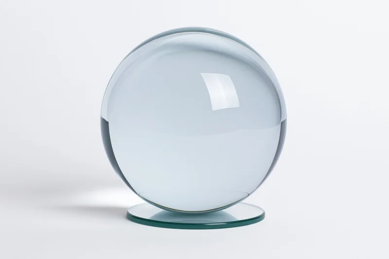 Clear glass crystal ball resting on a small circular glass base against a white background