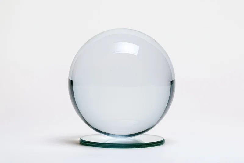 Clear glass crystal ball resting on a small circular glass base against a white background