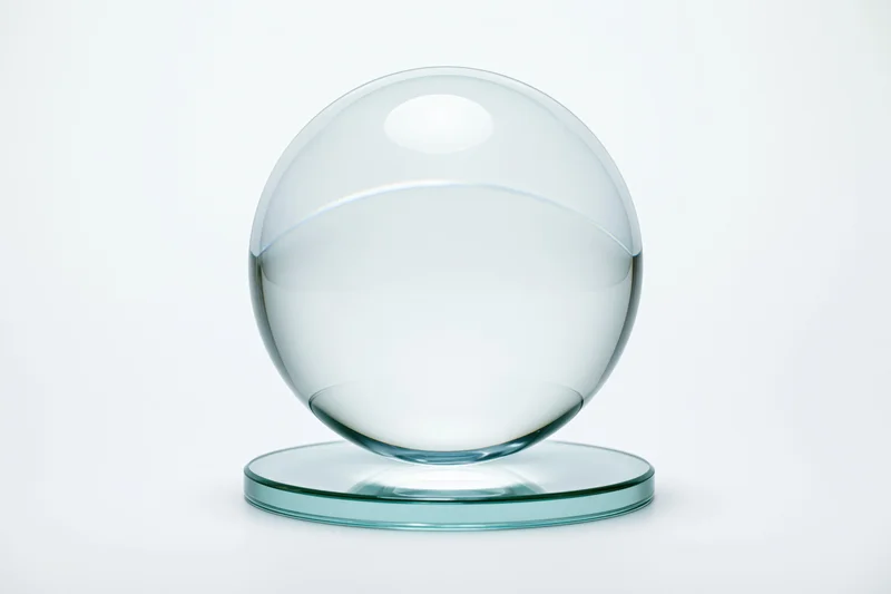 Clear glass crystal ball resting on a small circular glass base against white background
