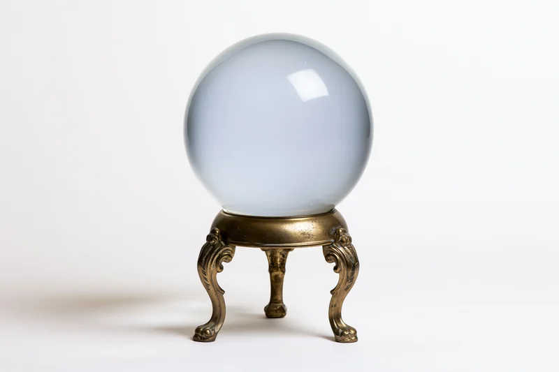 Clear glass crystal ball on ornate brass tripod stand against white background