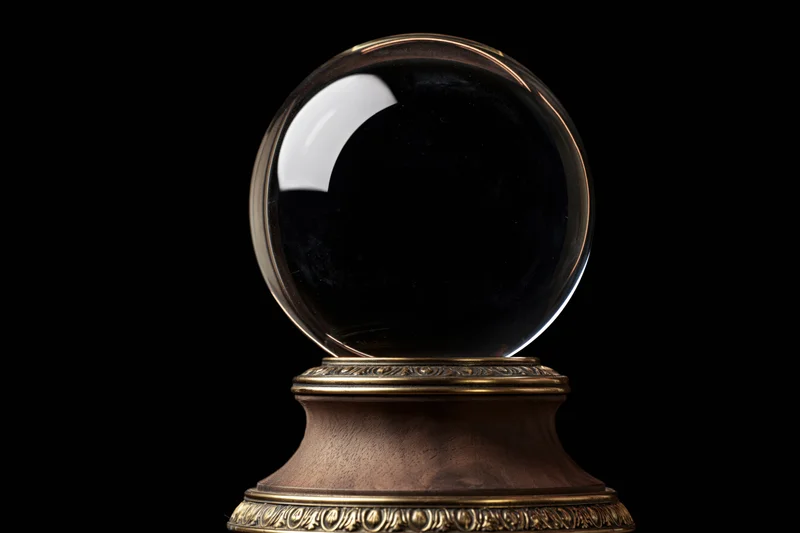 Clear glass crystal ball on ornate wooden base with brass accents against black background