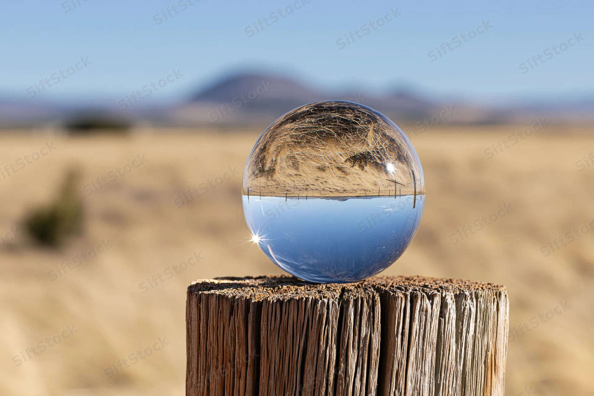 Clear glass crystal ball resting on weathered wooden post in desert landscape