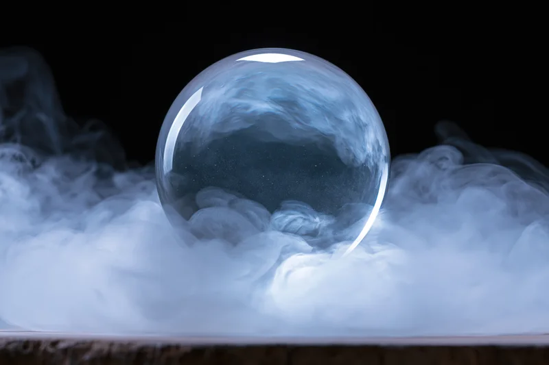Clear glass crystal ball resting on a bed of swirling smoke against a dark background