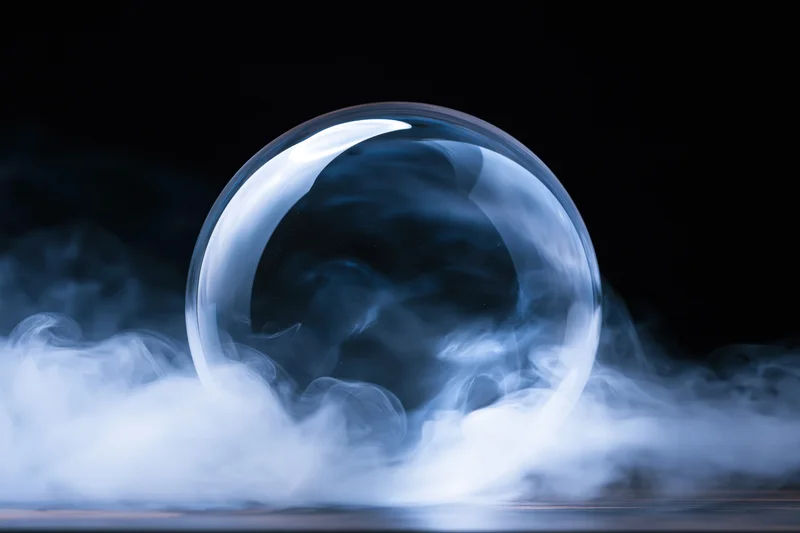 A clear glass crystal ball resting on a surface surrounded by swirling blue smoke against a dark background