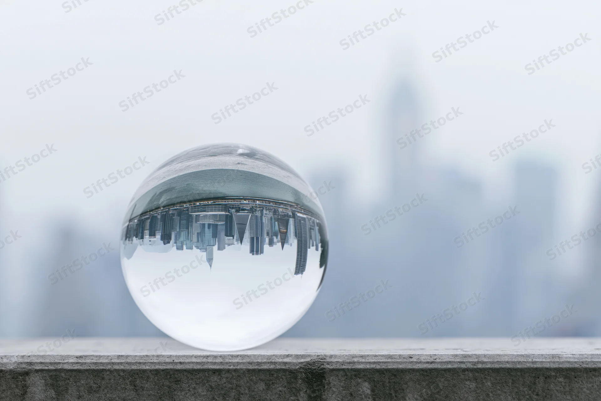 Clear glass lensball resting on concrete ledge reflecting inverted city skyline