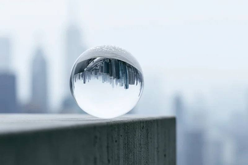 Clear glass lensball resting on concrete ledge reflecting inverted city skyline