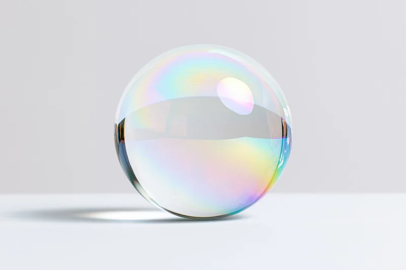 A transparent glass sphere with iridescent reflections resting on a white surface