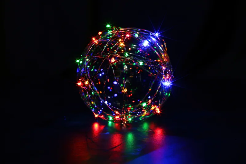 Multicolored led lights wrapped around a clear glass sphere on a dark reflective surface
