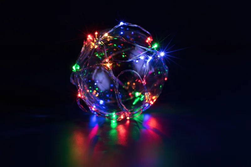 Multicolored led lights wrapped around a clear glass sphere on a dark reflective surface