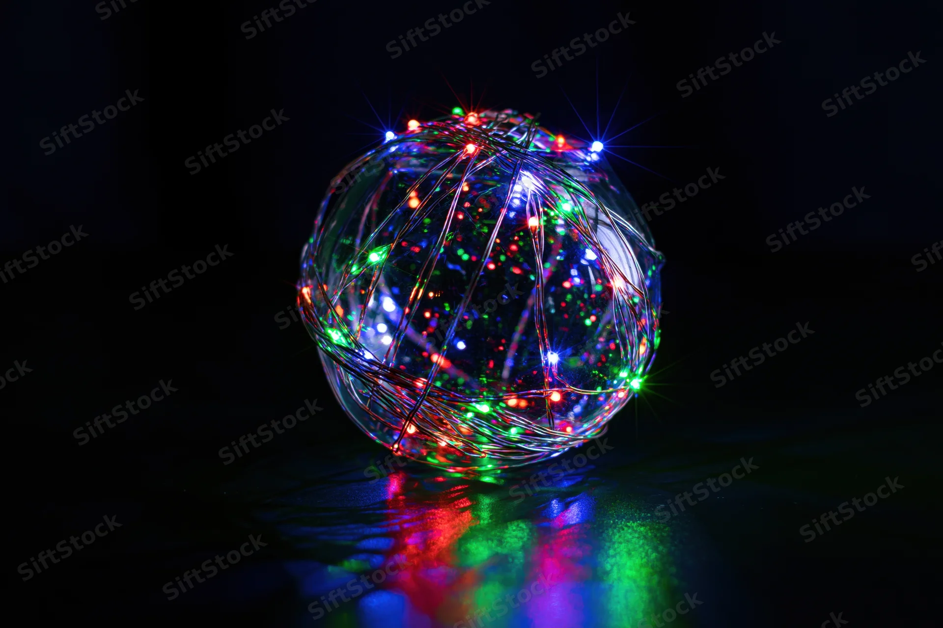 Clear glass sphere wrapped with multicolored led lights glowing on dark reflective surface