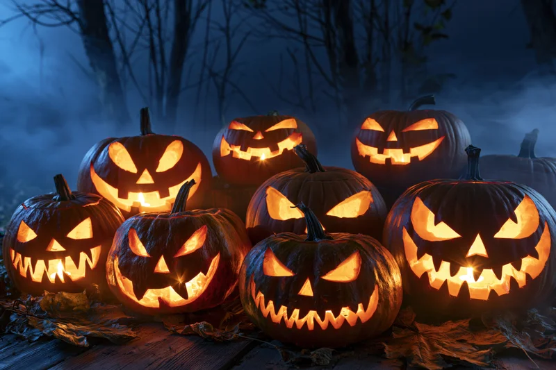 Carved jack-o-lanterns glowing in a foggy forest at night