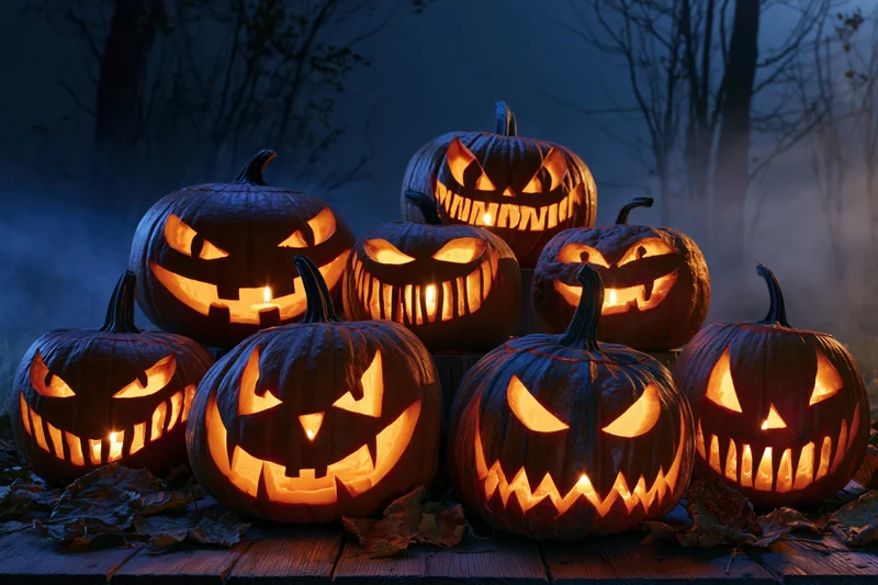 Carved jack-o-lanterns glowing on a wooden table in a misty forest at night